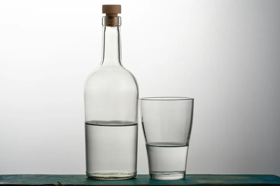 Glassflaske med kork og et vannglass, begge halvfulle med vann