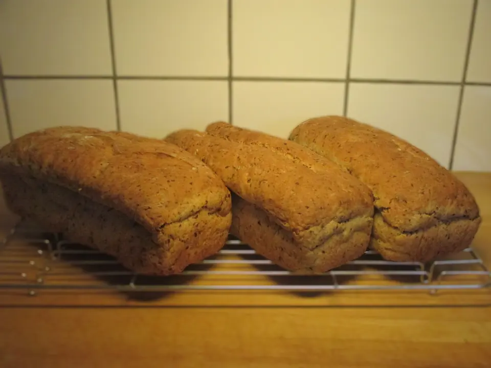 Tre hjemmebakte grove brød som avkjøles på en rist på kjøkkenbenken