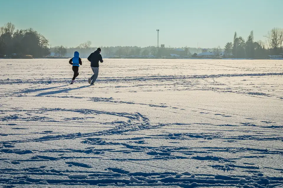 To personer jogger over en snødekt, islagt innsjø en klar vinterdag