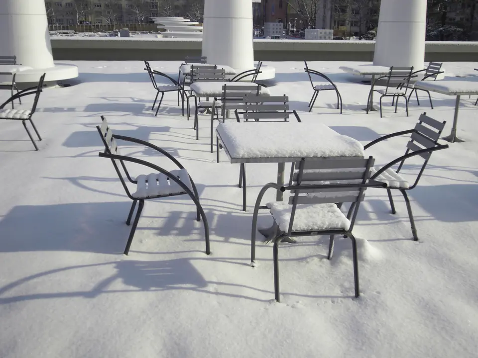 Snødekte metallstoler og bord på en terrasse i vintersol