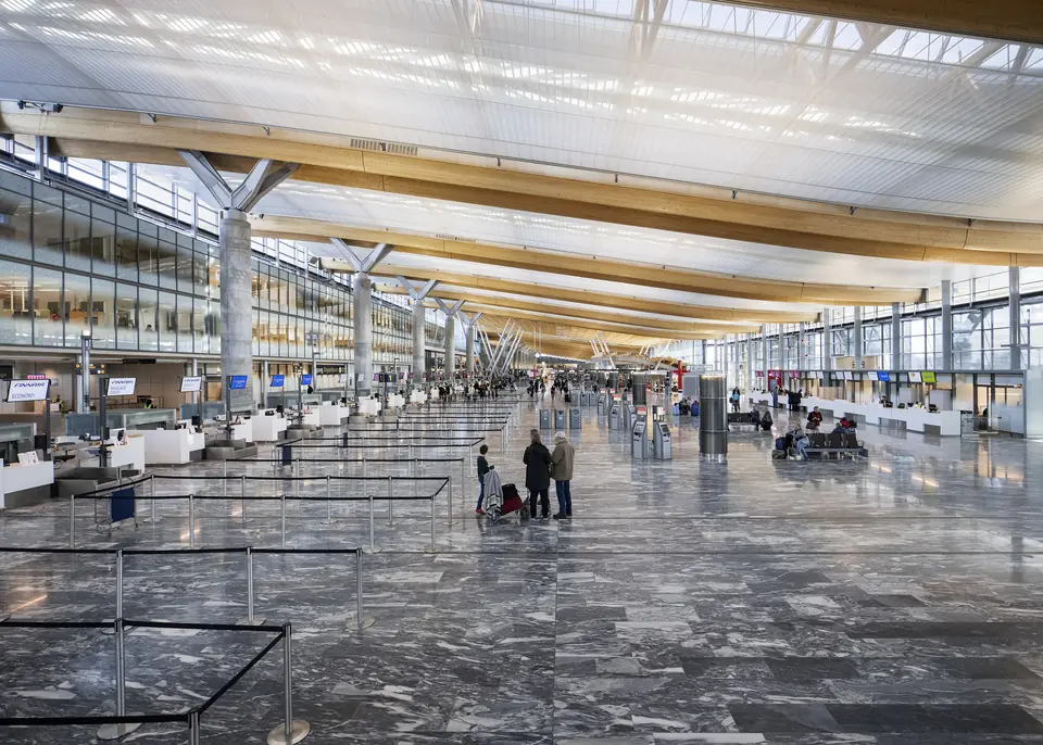 Innsjekkingshallen på Oslo lufthavn Gardermoen med høyt tretak og noen få reisende med bagasje