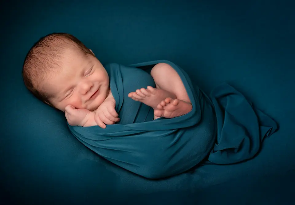 Nyfødt baby som sover og smiler, svøpt i et blågrønt teppe