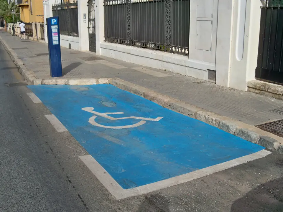 Blåmalt parkeringsplass med rullestolsymbol langs fortauet i en bygate