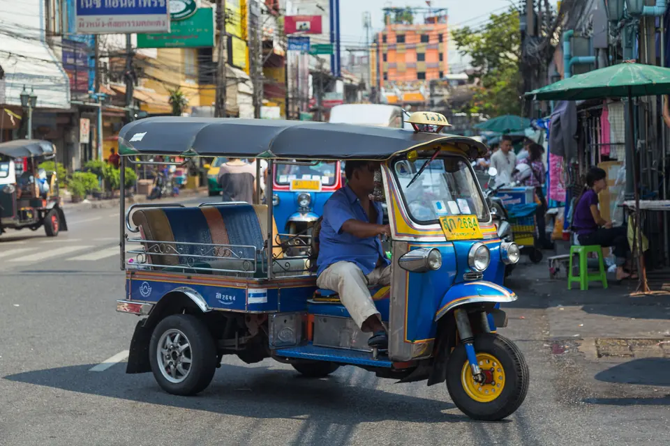 Blå tuk-tuk med taxiskilt på taket kjører gjennom en gate i Bangkok
