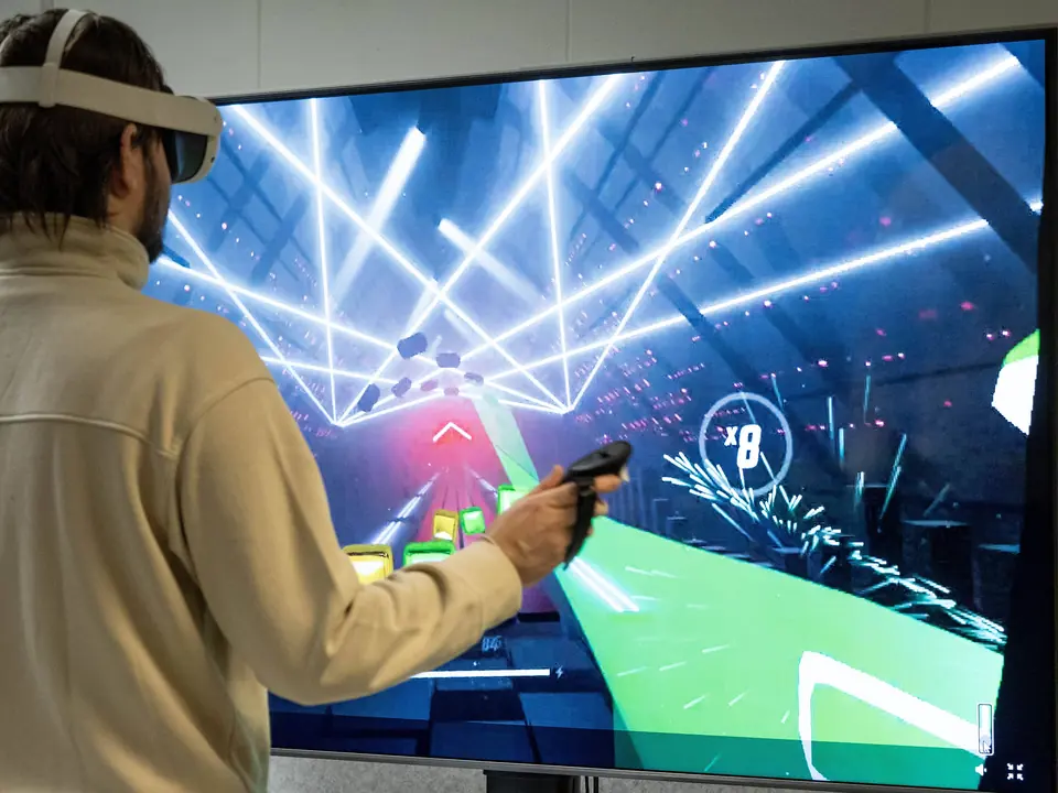 Person med VR-briller og håndkontroller spiller et lysende spill vist på en stor skjerm