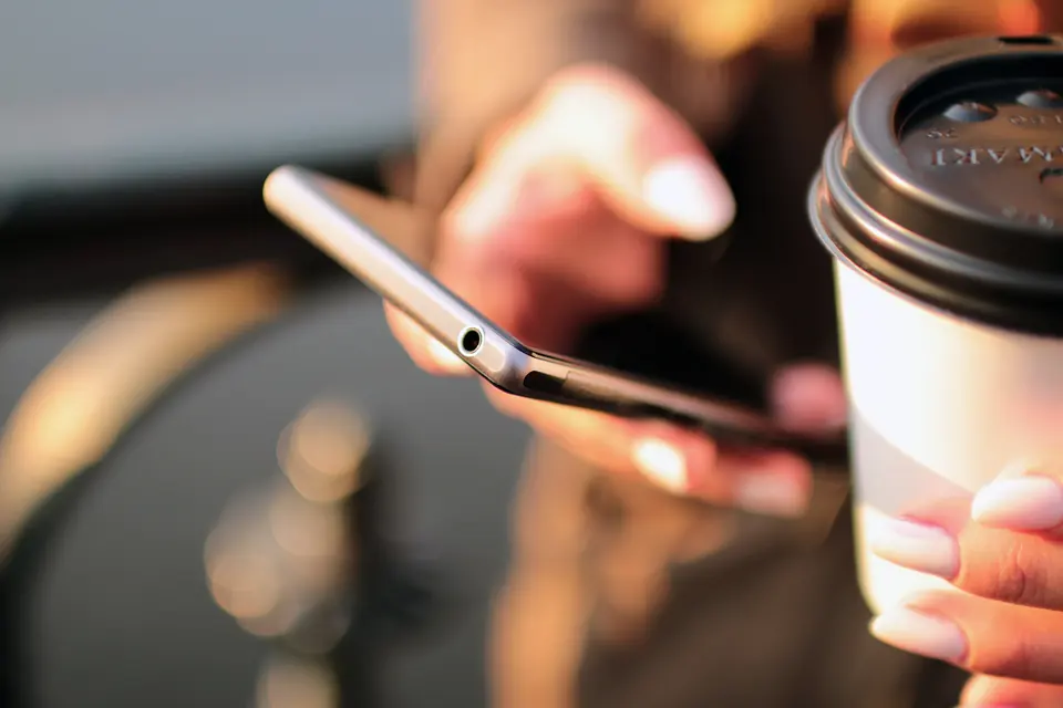 Hender som holder en mobiltelefon og en kaffekopp i varmt motlys