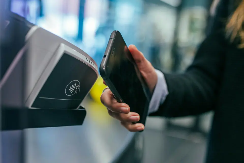 Hånd som holder en mobiltelefon mot en betalingsterminal for kontaktløs betaling